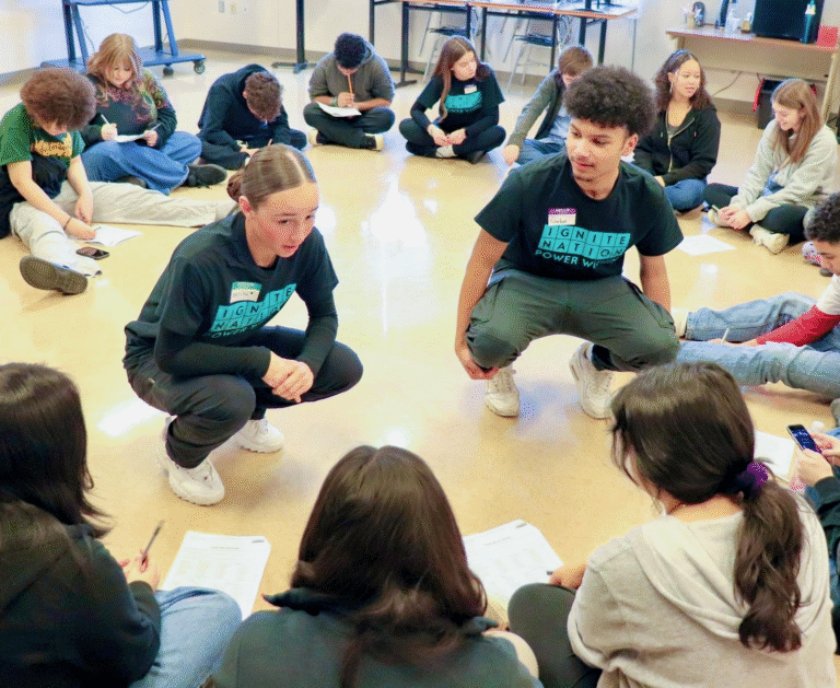 Mentors lead a circle discussion on the floor, organizing ninth-graders for the activity.